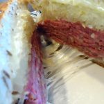 close up of a rueben sandwich with strings of cheese between the 2 halves