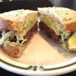 savory pastrami sandwich on rye bread with a pickle wedge on the side