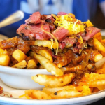 Pastrami on top of chili cheese fries piled high on a plate